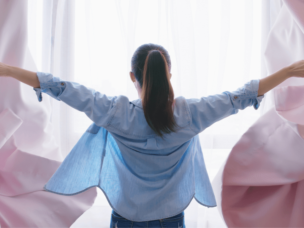 Frau öffnet Vorhänge ins Licht – Symbol für Neuanfang und Transformation im Coaching bei Kregel Coaching
