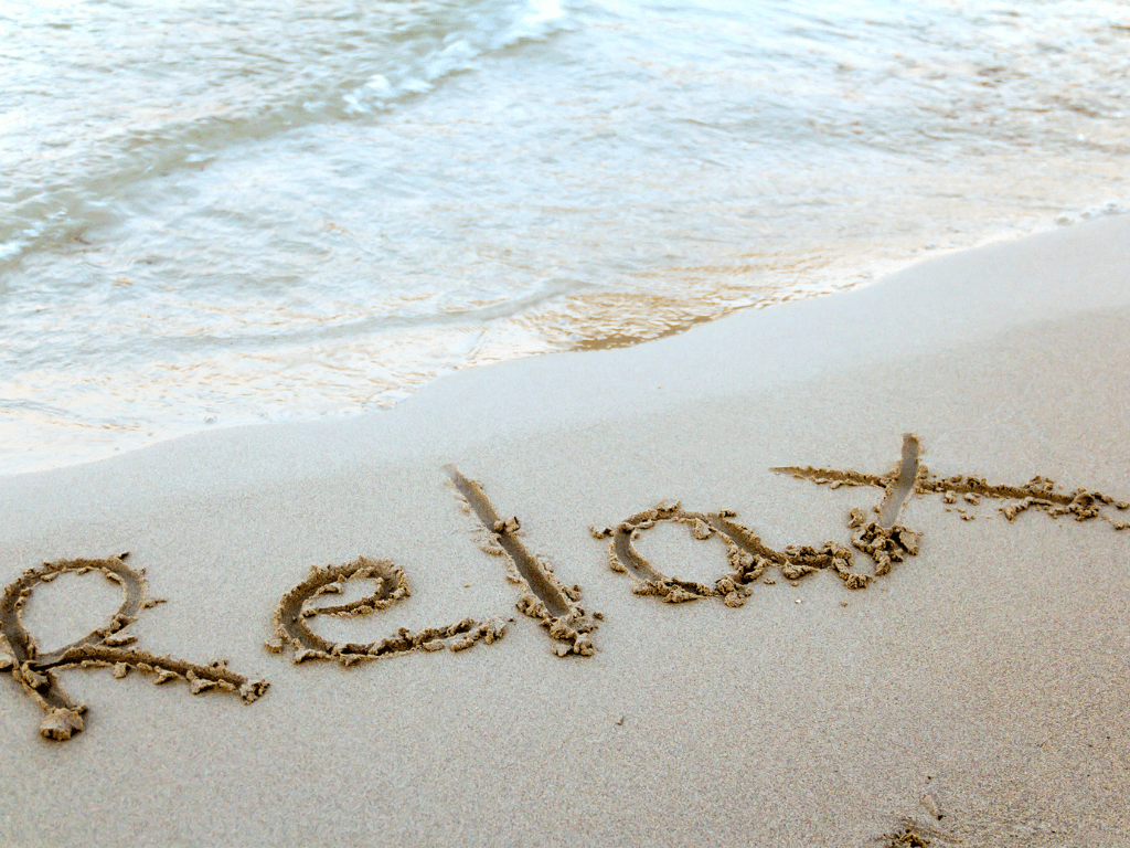 Wort ‚Relax‘ im Sand am Meer, Symbol für Entspannung und Gelassenheit
