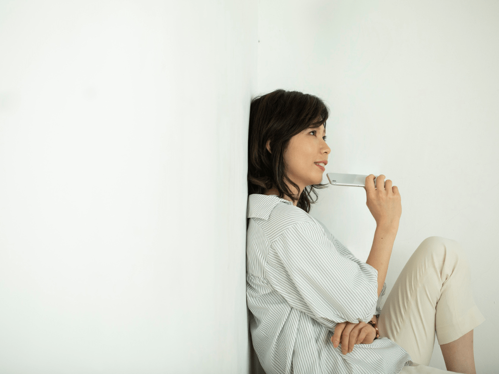 rau sitzt ruhig angelehnt an einer Wand und hält nachdenklich ein Handy in der Hand