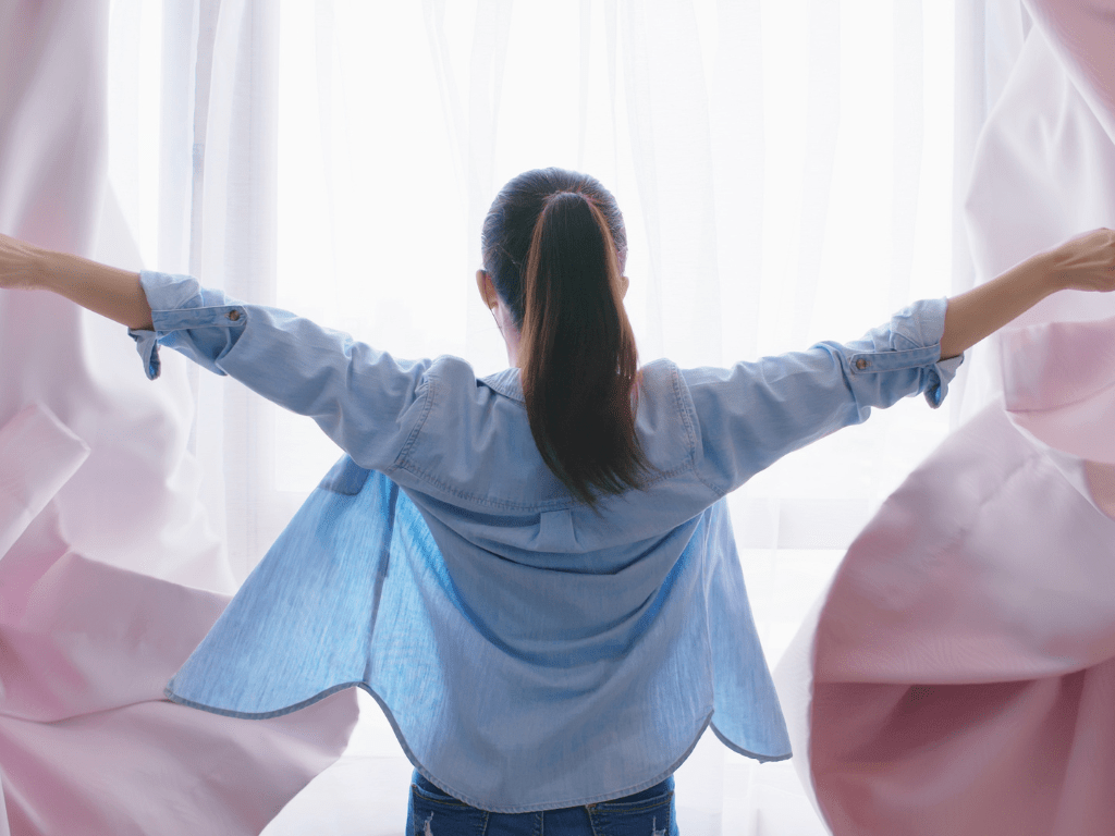 Person steht vor einem Fenster und zieht die Vorhänge auseinander – symbolisch für erste Orientierung und Klarheit beim Imposter-Syndrom