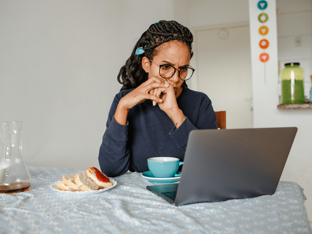 Frau sitzt allein an einem Tisch mit Laptop und wirkt nachdenklich