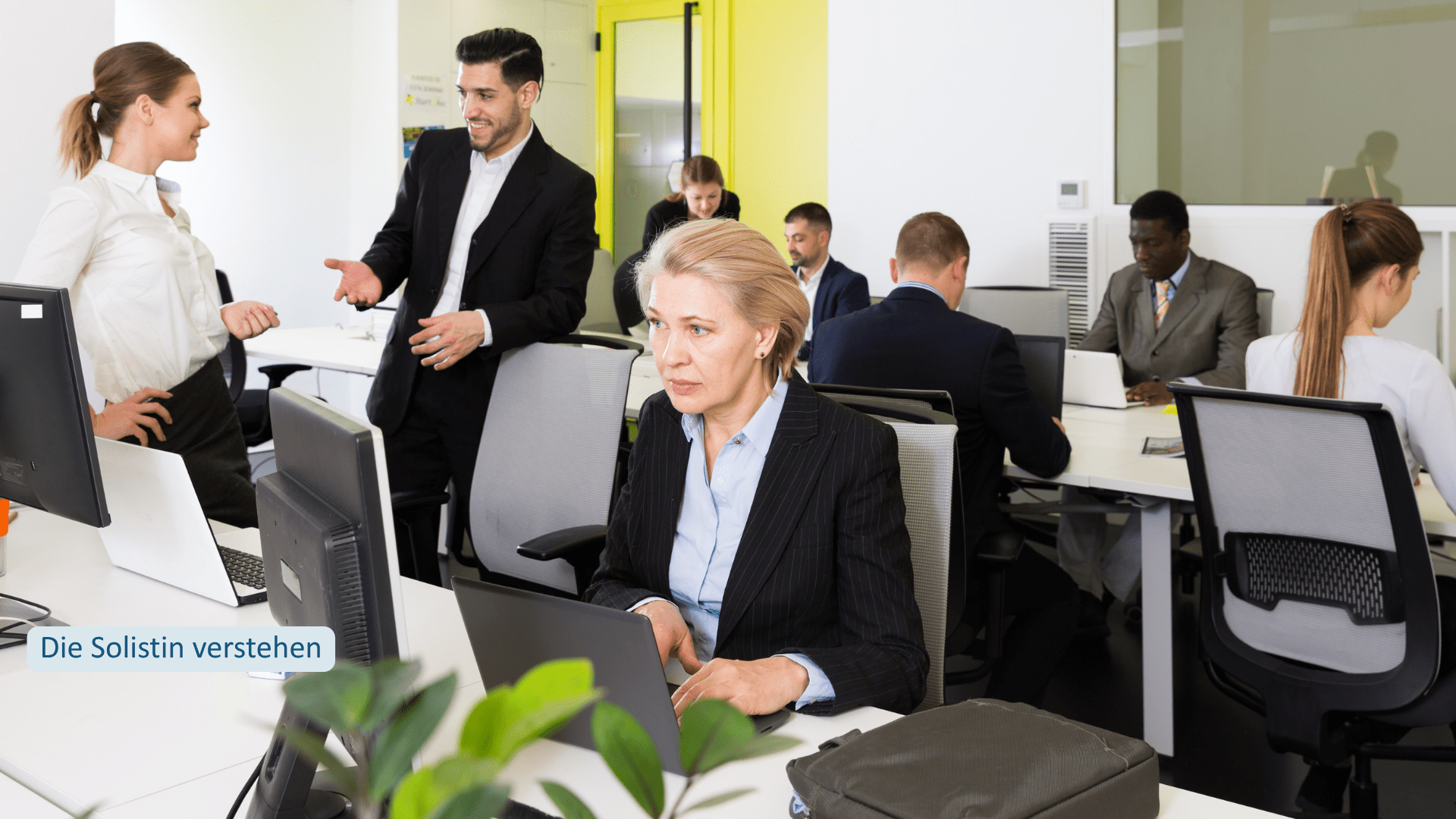 Frau arbeitet eigenständig im Büro, während andere im Team zusammenarbeiten – Solistinnenmuster beim Imposter-Syndrom